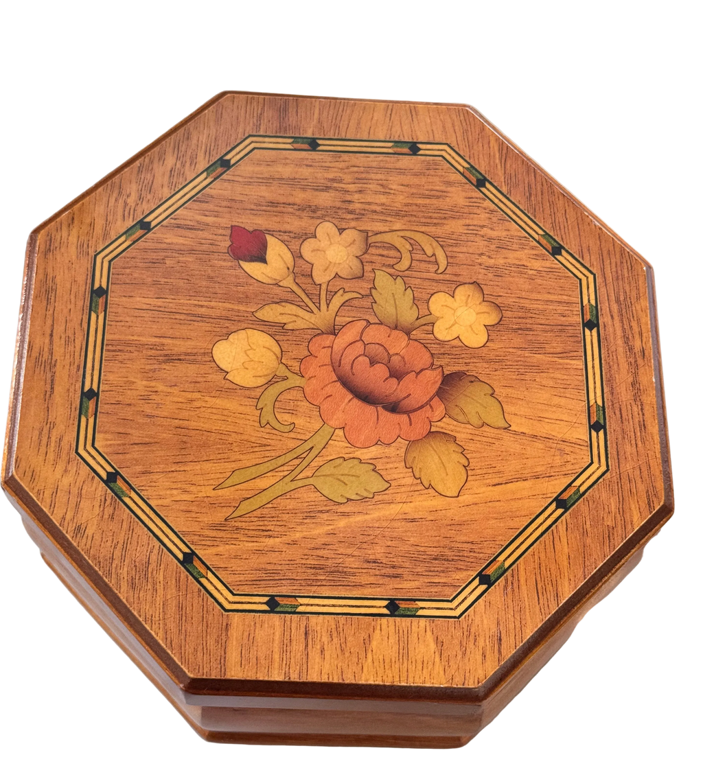 An octagonal wooden box lid featuring a detailed floral inlay design in shades of orange, yellow, and green on a warm brown wood grain background.