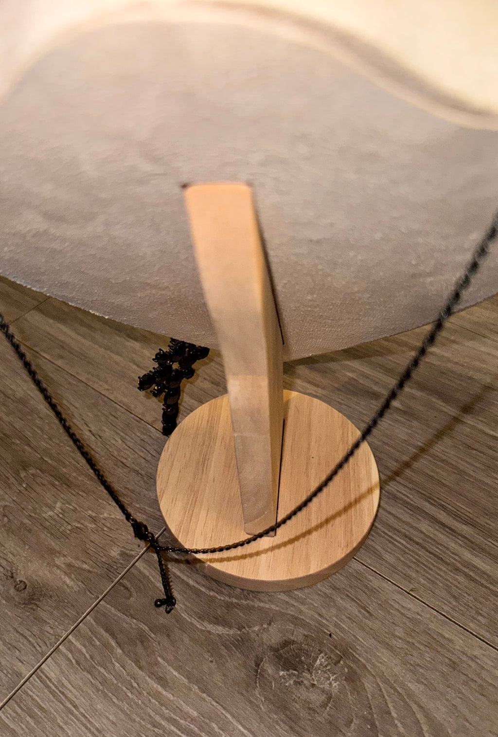 A close-up of a necklace displayed on a wooden stand, with a black chain necklace draped over a light wood base on a gray wood-look floor.. Displaying chain length. 