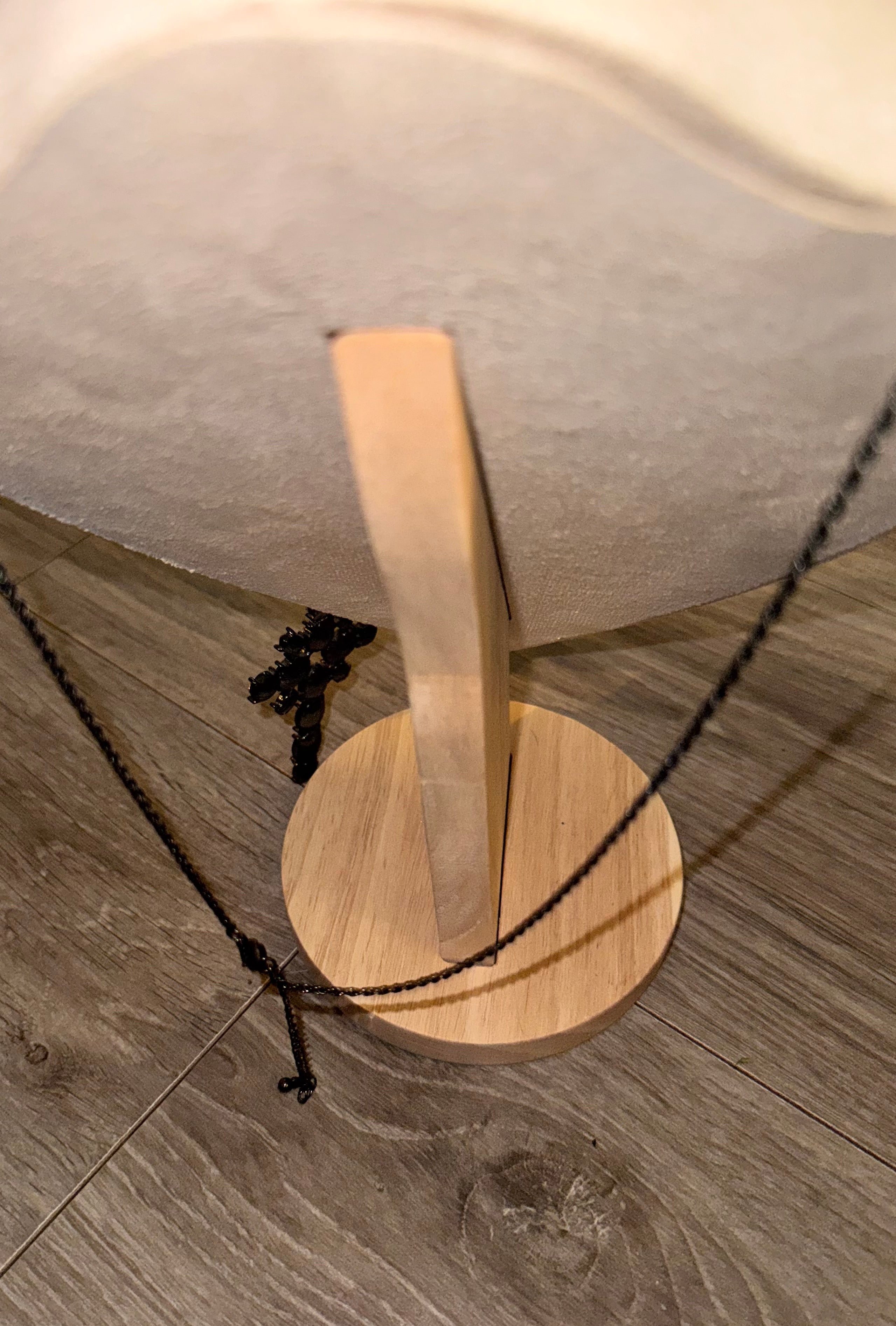 A close-up of a necklace displayed on a wooden stand, with a black chain necklace draped over a light wood base on a gray wood-look floor.. Displaying chain length. 