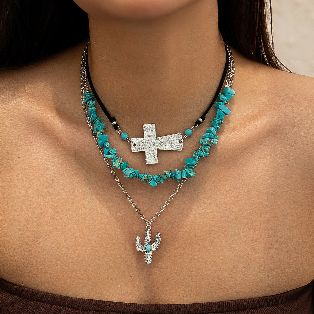 Multi-layered 3 layers necklace with a cross laid on its side. on the first. not a tight choker but on a cord with the cross. The next necklace is Turquoise colour chips and the third a chain with a cactus