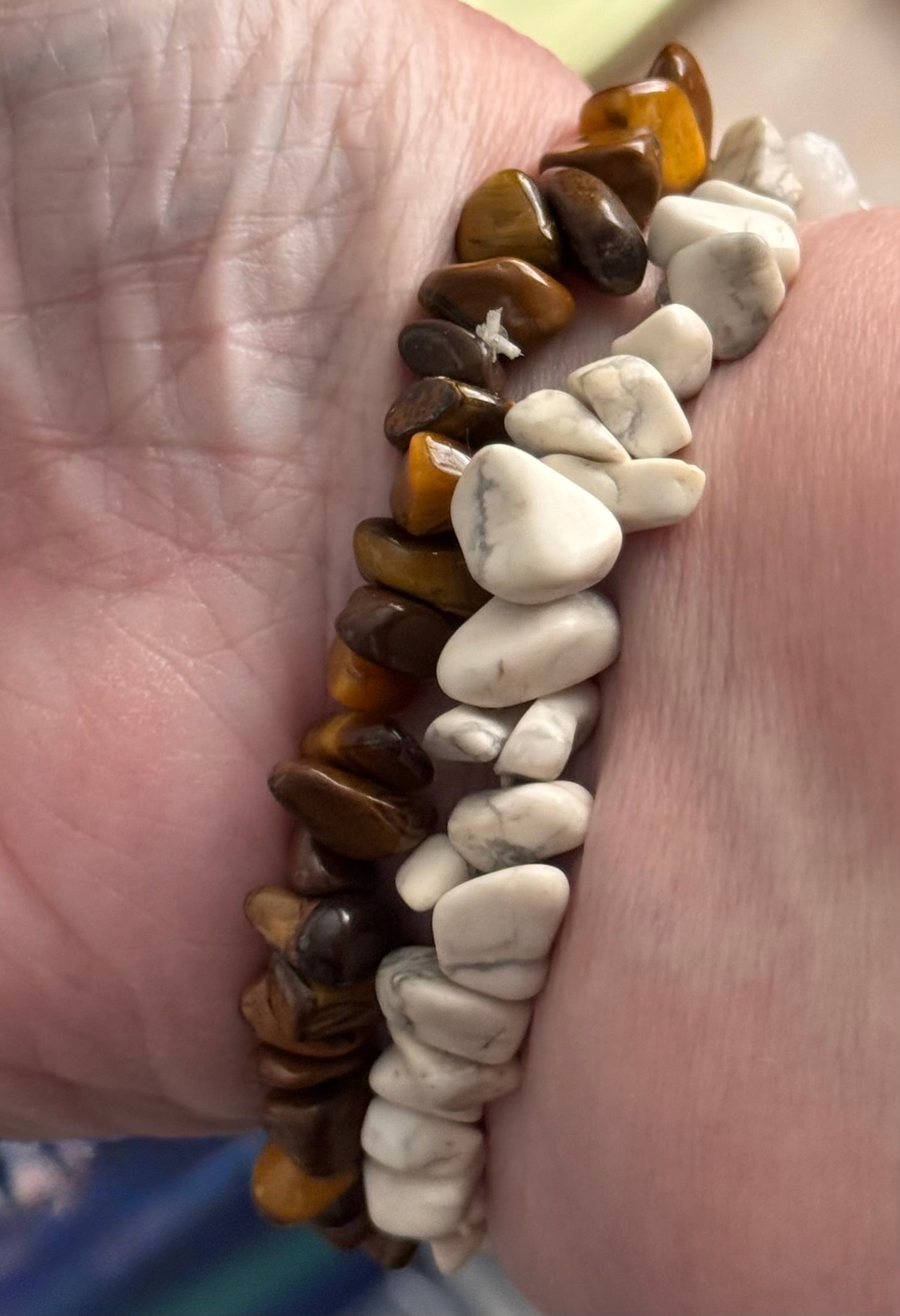 A close-up of a person's wrist wearing two beaded stretch bracelets. One bracelet features polished brown and golden tiger's eye stones, while the other features smooth white river stones.