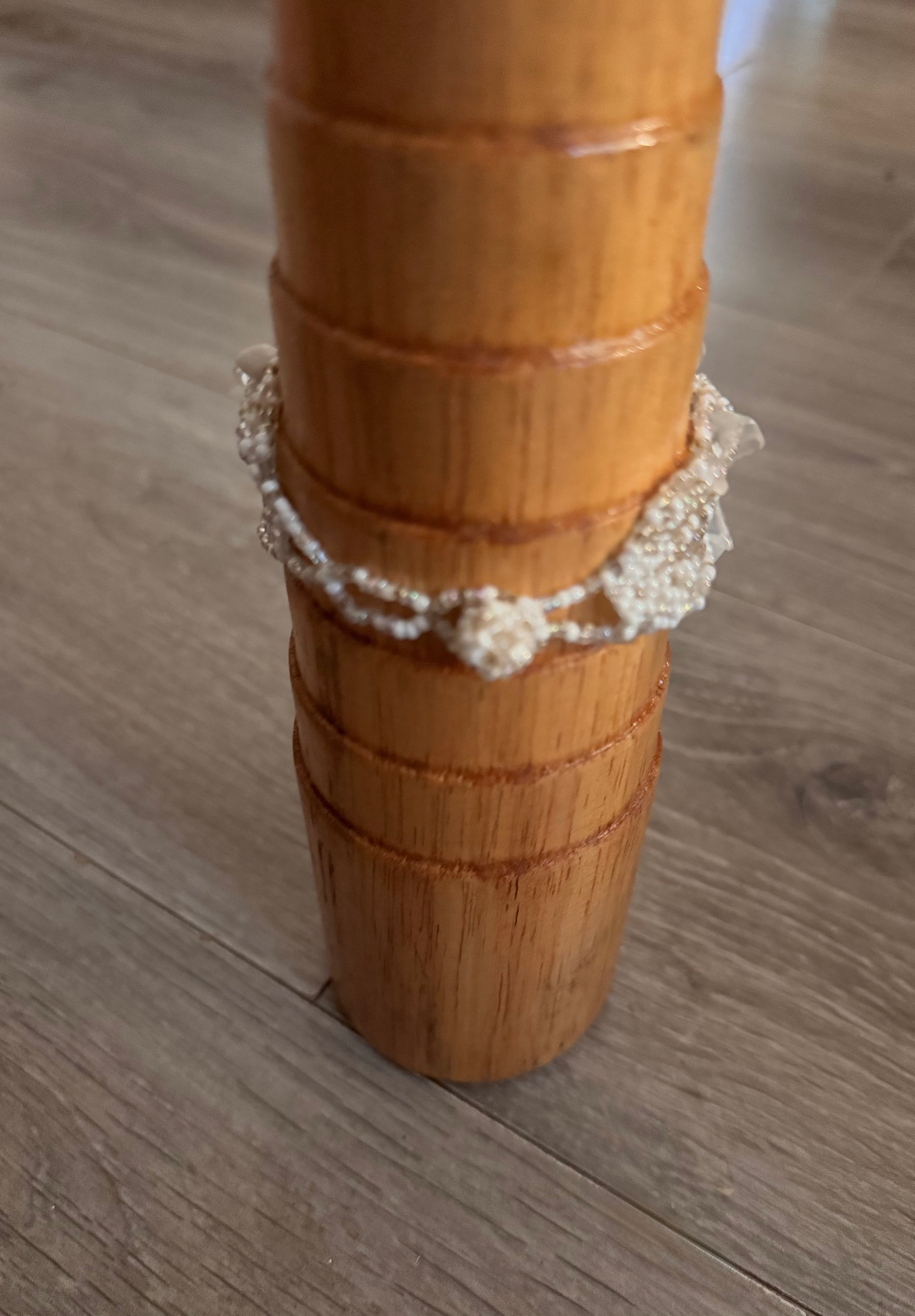A beaded bracelet with white and beige and opaline beads and floral type unique clasp, displayed on a wooden bracelet mandrel over a gray wood-look floor.