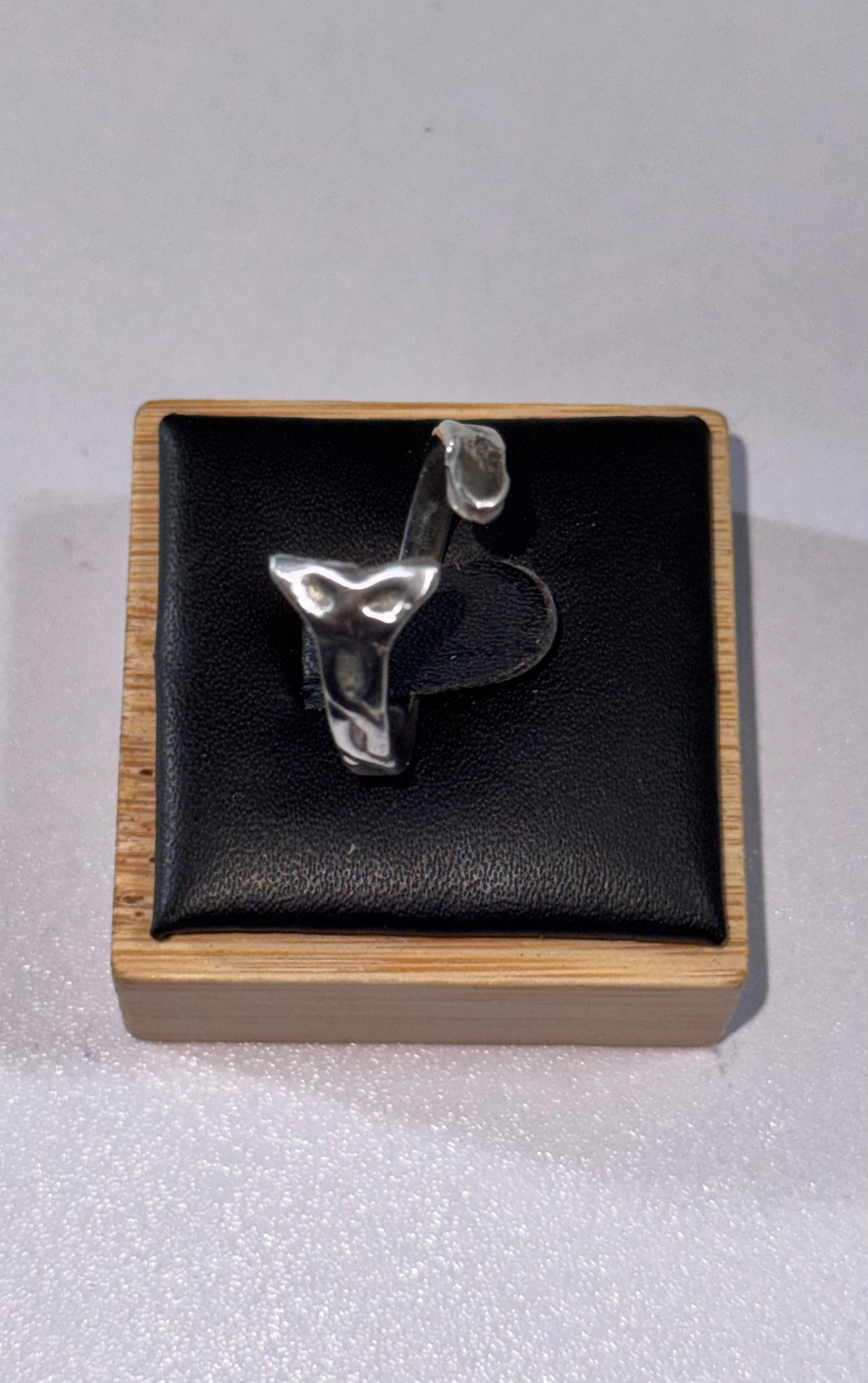 A sterling silver s925 abstract sea snake sculptural ring displayed on a black cushion inside a square wooden presentation box, photographed against a light gray background.