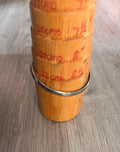 A bracelet mandrel with red handwritten measurements, displaying a silver toned non precious metal bangle, on a gray wood-look floor.