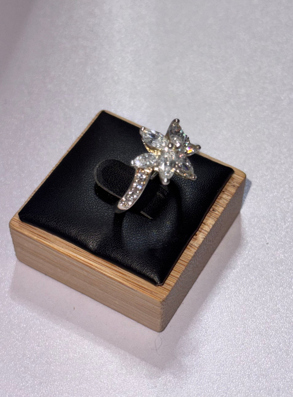 A sterling silver star-shaped ring set with clear crystals, displayed on a black cushion inside a light wood jewelry box against a light gray background. Size Q 1/2
