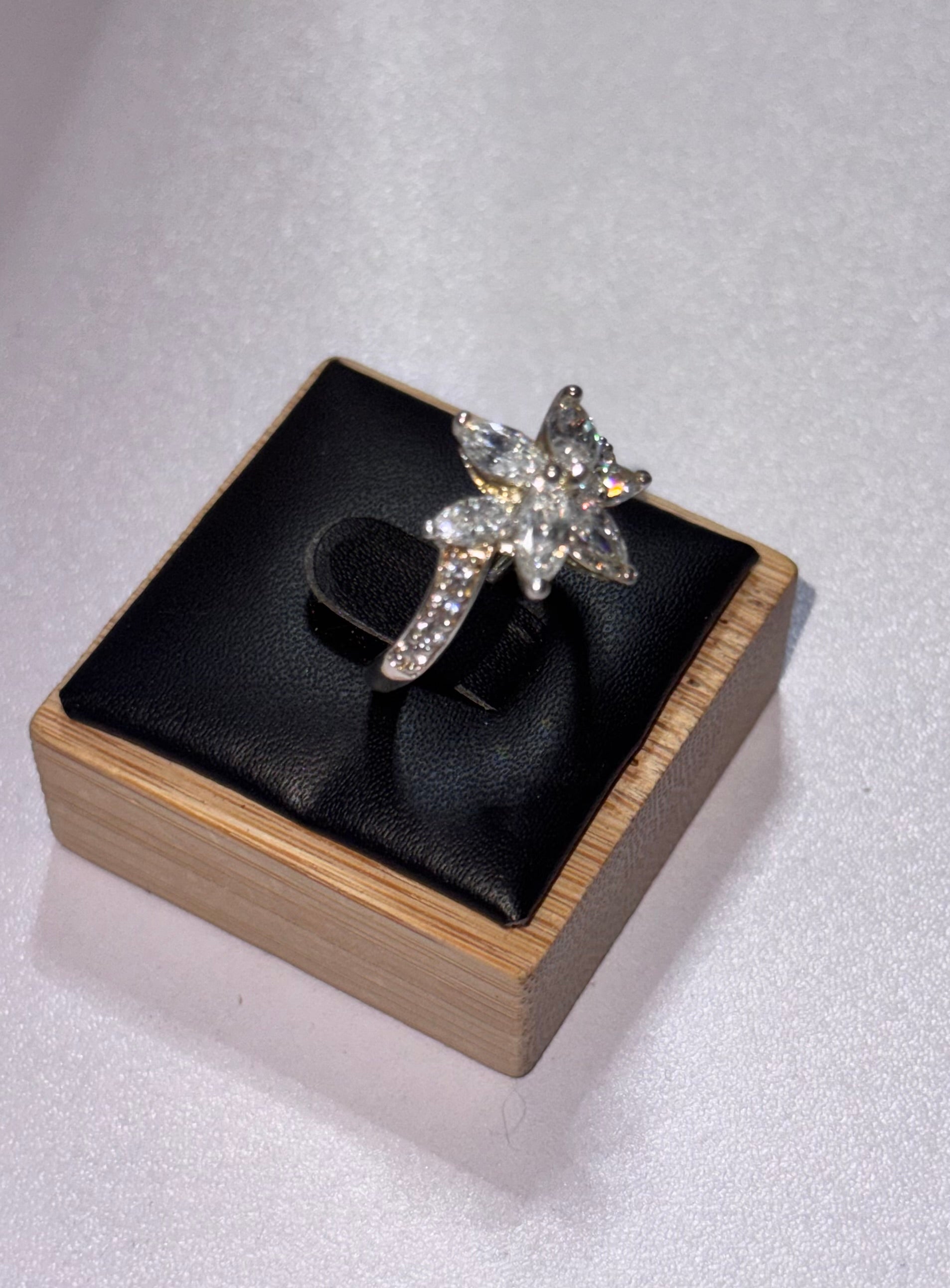 A sterling silver star-shaped ring set with clear crystals, displayed on a black cushion inside a light wood jewelry box against a light gray background. Size Q 1/2