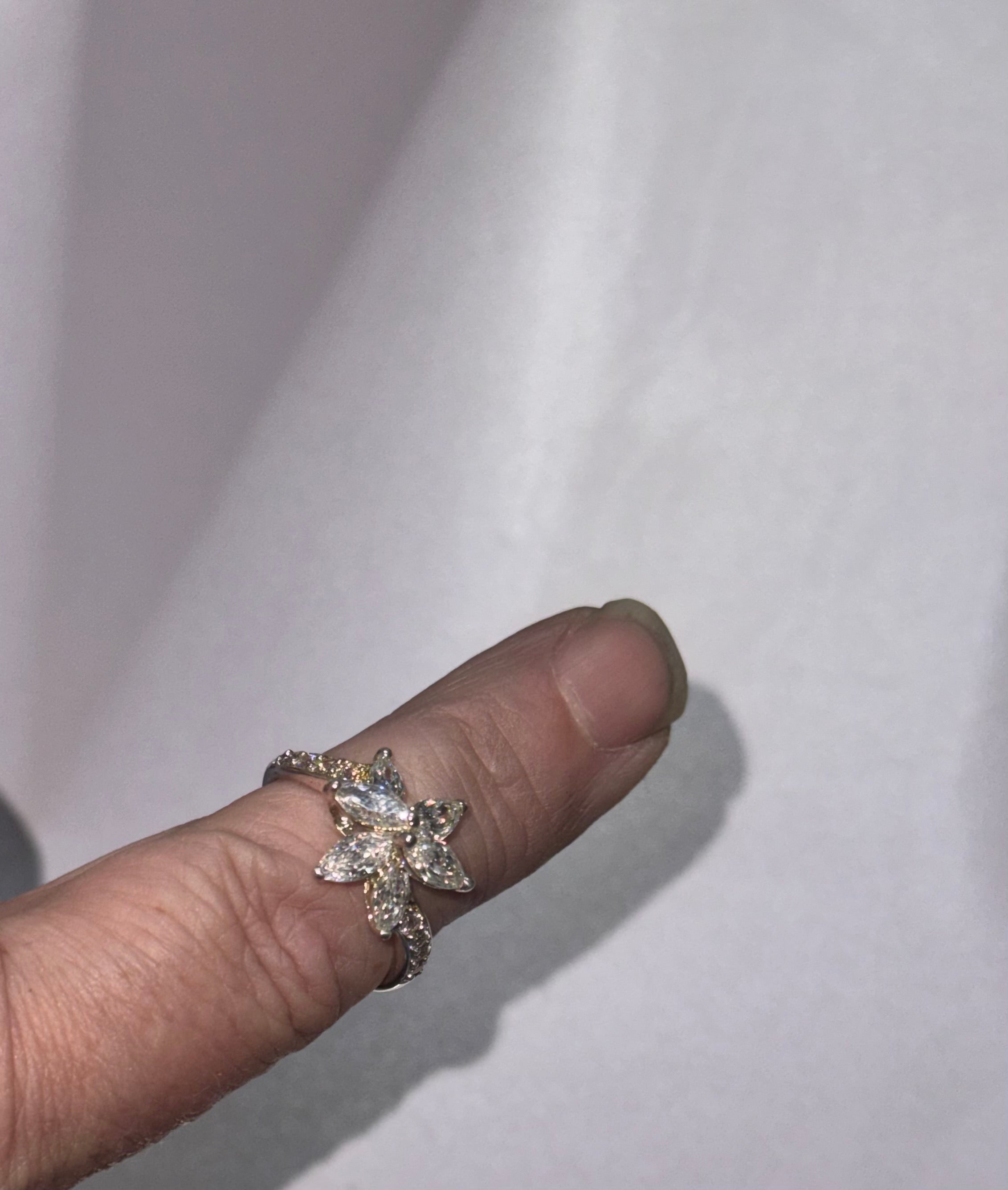 A sterling silver ring with a star-shaped floral cluster of clear stones, worn on a person's finger against a light gray fabric background.