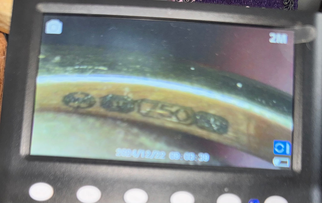 A close-up of a handheld electronic device with a small screen showing the magnified view of the hallmark on a curved metallic surface.