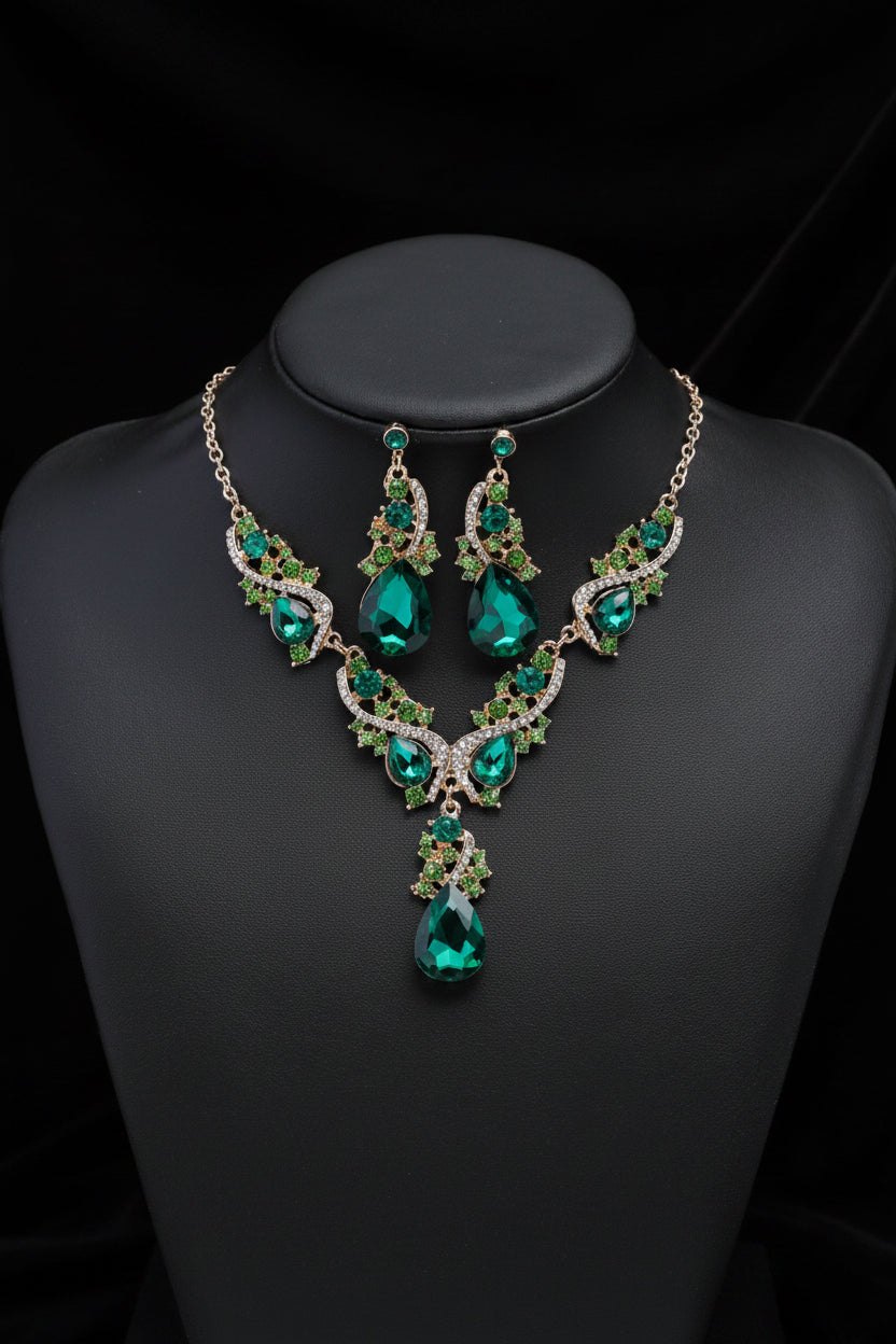 A green crystal jewelry set including a necklace and matching earrings, displayed on a black mannequin bust against a black background.