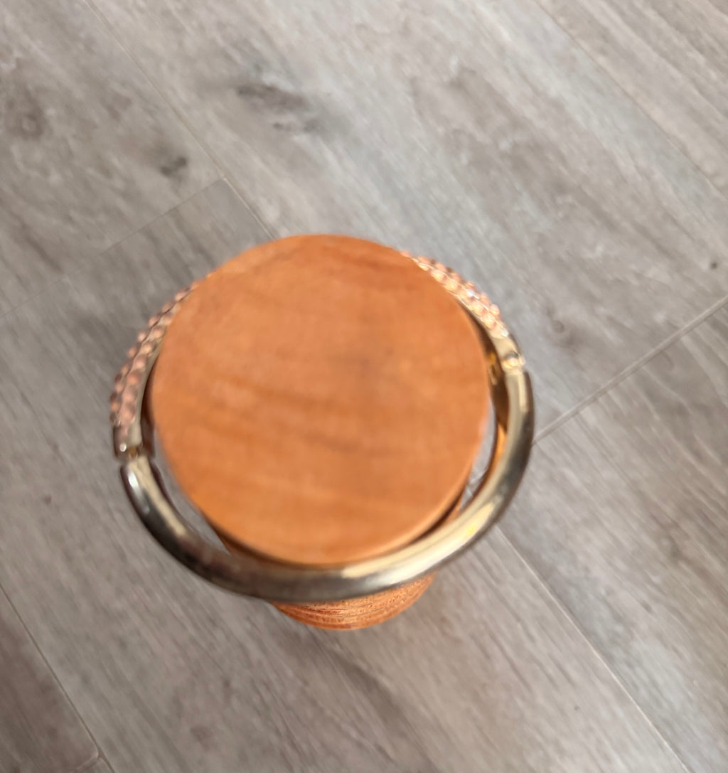 A top-down view of the round wooden mandrel with the bracelet at the top, showing the bracelet is oval and the mandrel is round. This is set on a grey wood-look floor background.