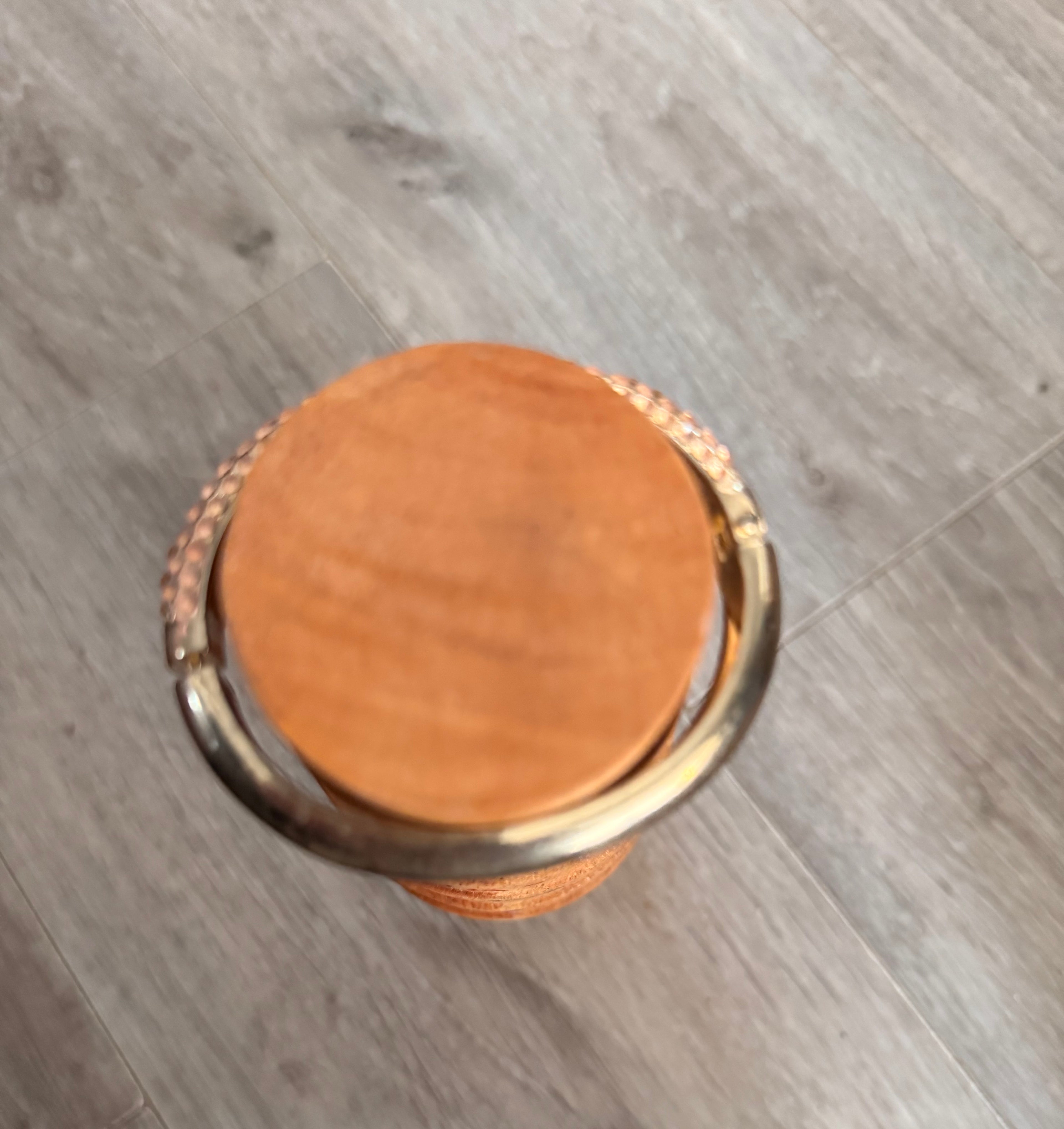 A top-down view of the round wooden mandrel with the bracelet at the top, showing the bracelet is oval and the mandrel is round. This is set on a grey wood-look floor background.