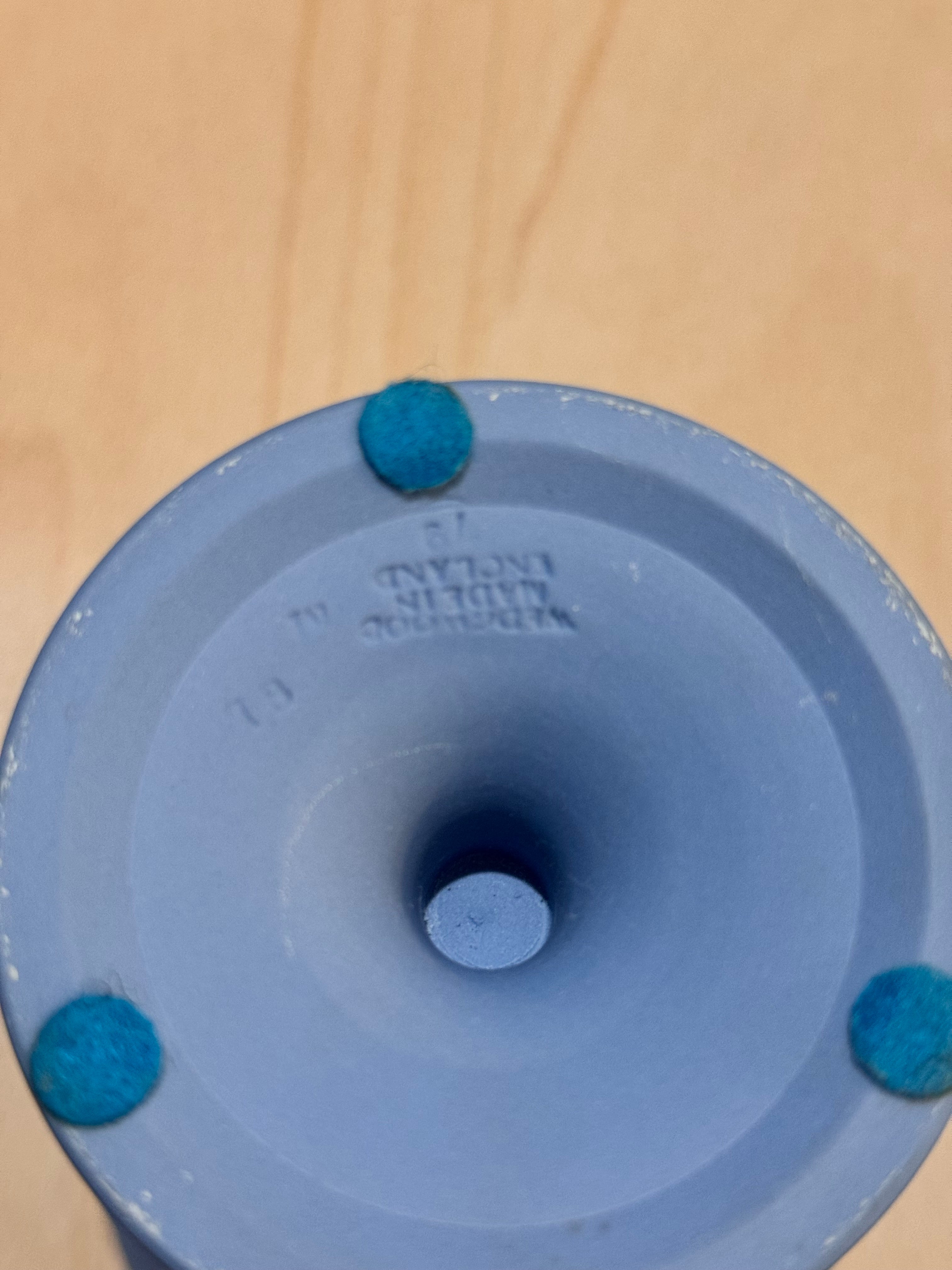 Close-up of the bottom of a blue ceramic vase or planter with three small blue feet, photographed on a light wood surface. Saying Wedgewood Made in England