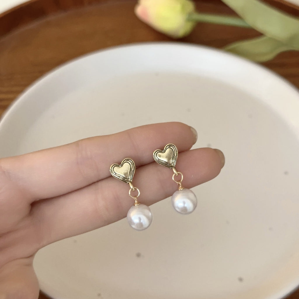 Both earrings dangling between elegant fingers on a white background. There is a tulip in the distance.