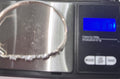 A silver-toned beaded bracelet is shown on a digital scale with a black display screen and metallic platform. Displaying the weight of 11.7 grams