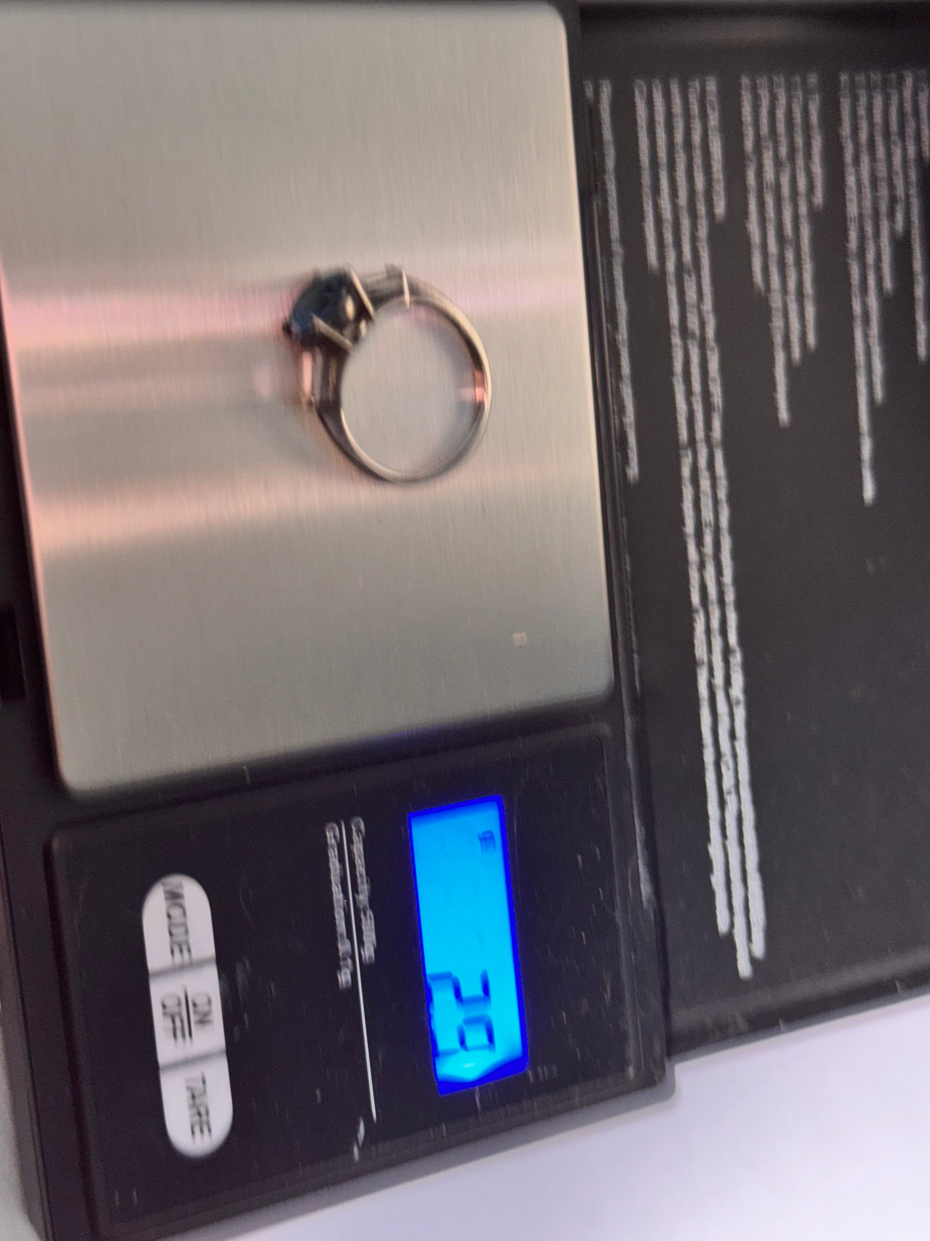 A silver-toned ring with a dark blue stone is shown on a digital scale displaying a weight of 2.9 grams.