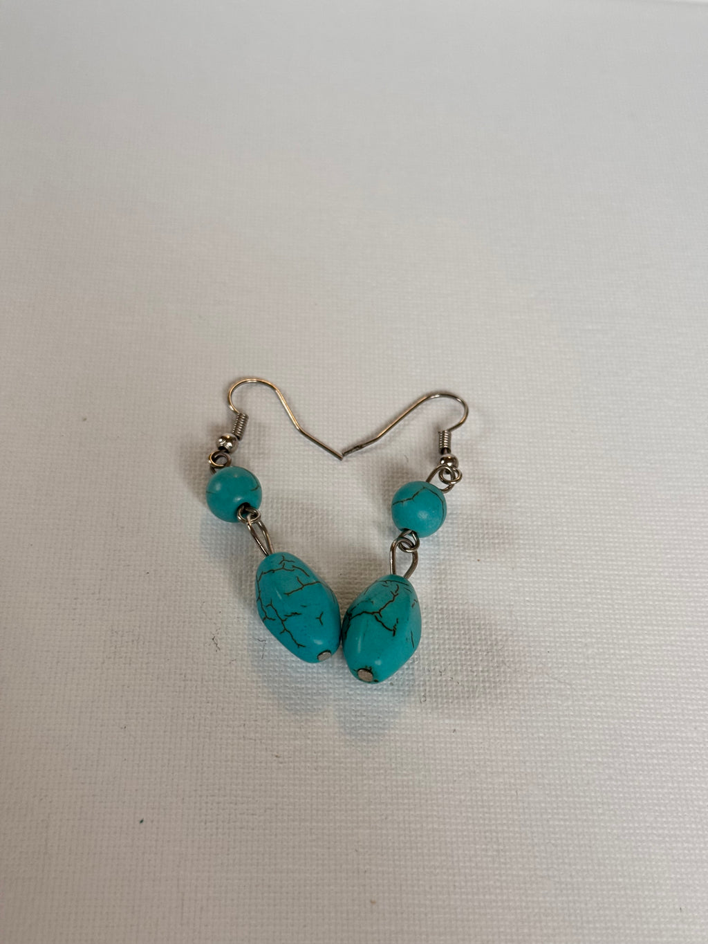 A pair of dangle earrings featuring turquoise-blue marbled beads and small round turquoise beads on silver-tone fishhook wires, displayed on a textured white background.