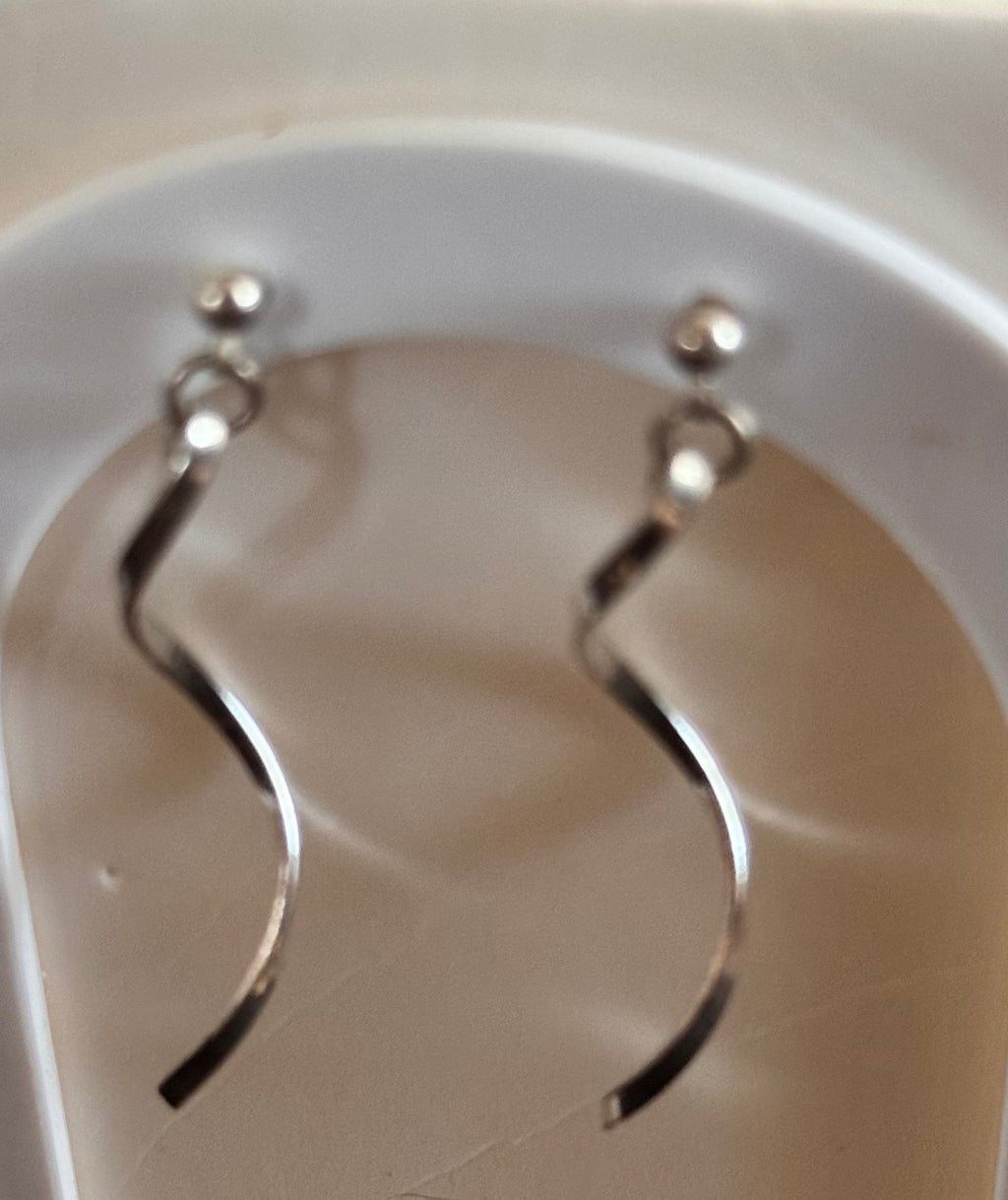 A pair of silver-toned wavy dangle earrings displayed on a white arch stand.