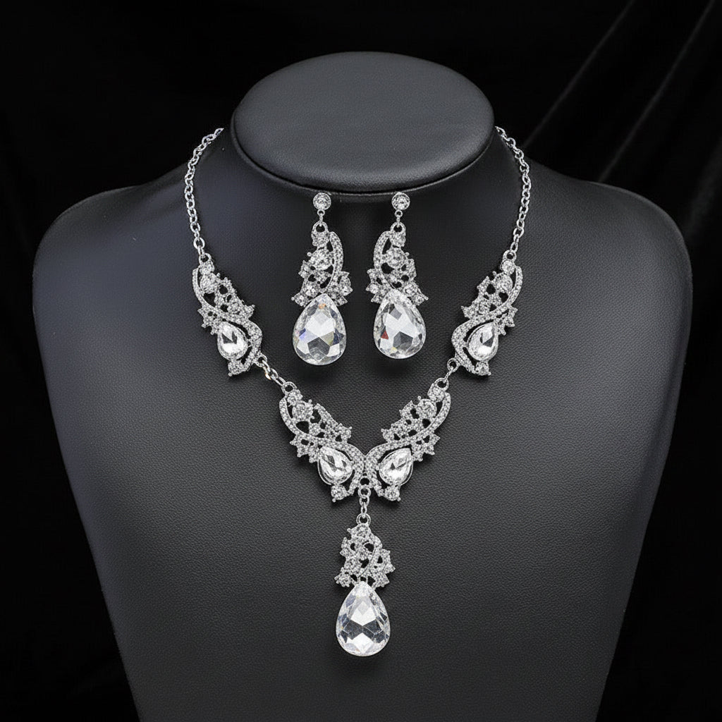 The vintage style silver-tone necklace and earrings set on a black mannequin bust with a dark background. The lovely clear crystal teardrops are surrounded by smaller round ones and this makes for a stunning and elegant statement jewelry set.