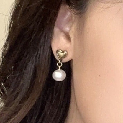 Close up of Heart & faux pearl earrings in an earlobe